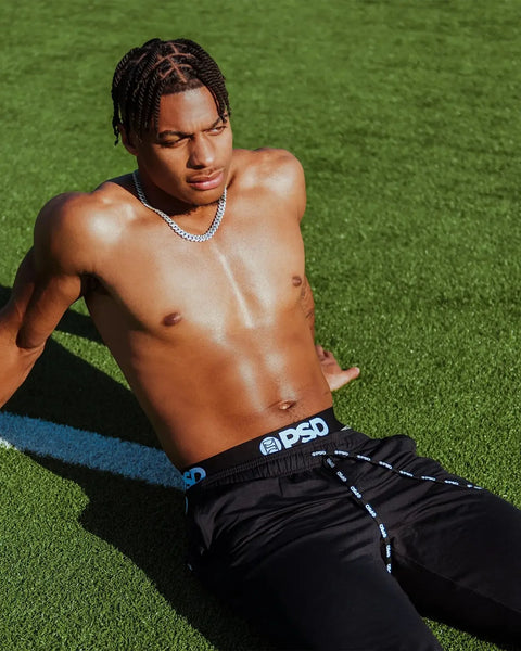 Black joggers with blue and white branded waistband, shown on model against green background.