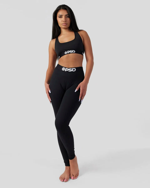 Woman wearing black sports bra and matching black leggings with PSD branding on waistbands.