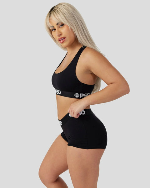 Woman wearing black racerback sports bra and matching shorts with PSD waistband logo.