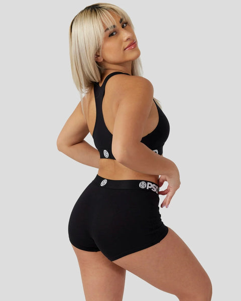 Woman wearing black sports bra and shorts with branded waistband, shown from back at angle.