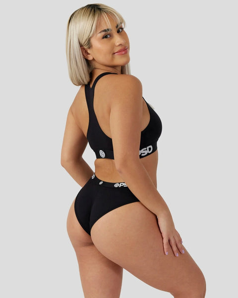 Woman wearing black sports bra and matching briefs with logo waistband, shown from back angle.