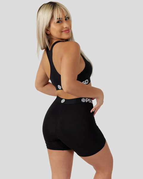 Woman wearing black sleeveless sports bra and matching black shorts with brand logo detail on waistband.