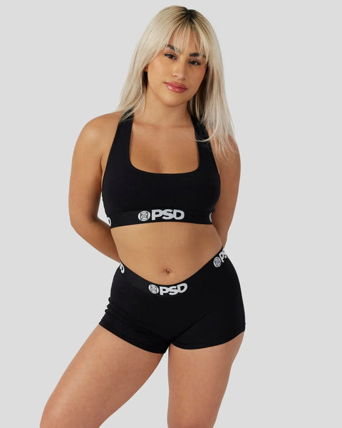 Woman wearing black sports bra and shorts with PSD branding on elastic waistbands.
