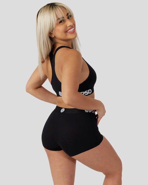 Woman wearing black racerback sports bra and matching shorts with brand logo detail.