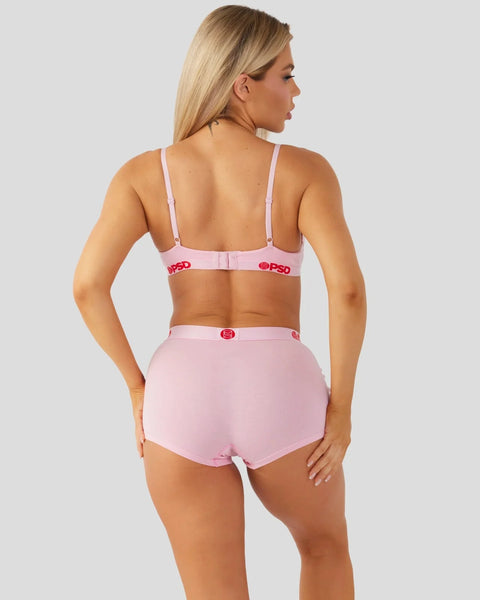 Woman wearing pink bra and high-waisted briefs with red logo detailing, shown from back view.
