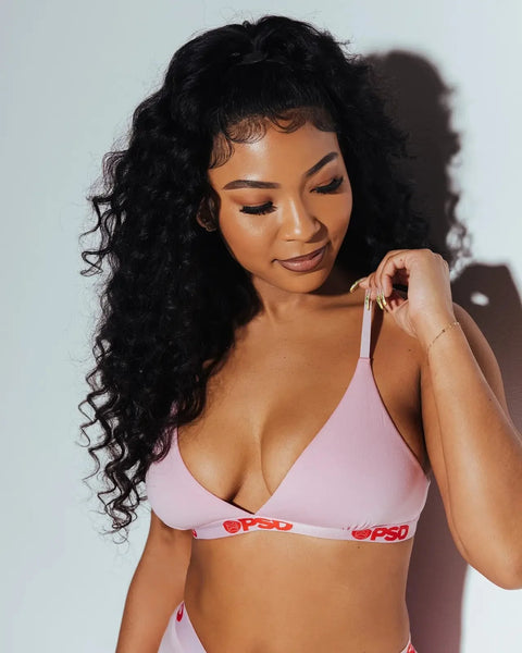 Pink modal sports bra with logo waistband, worn by model with curled black hair against white background.