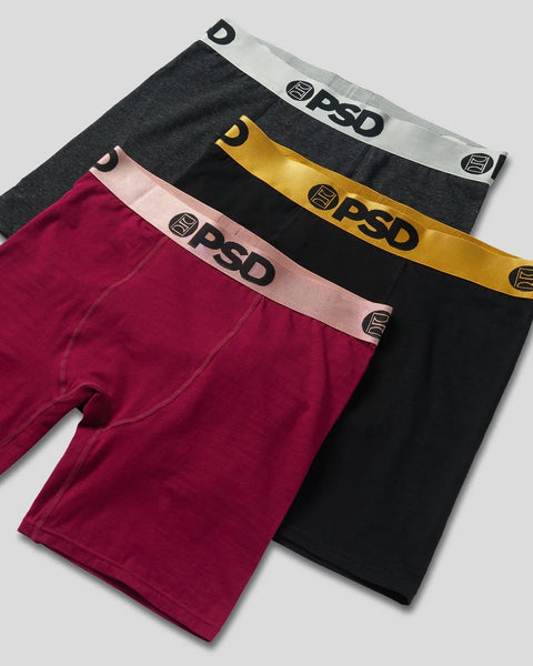 Three PSD boxer briefs in burgundy, black, and gold with metallic waistbands displayed overlapped.