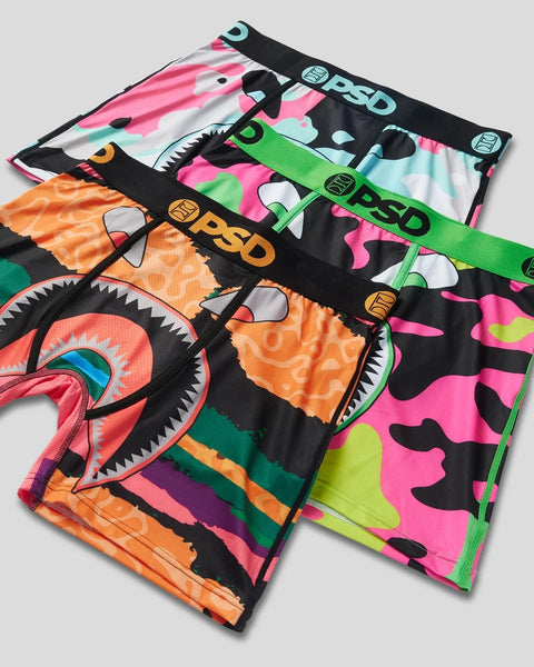 Three underwear briefs in neon camo patterns: pink/cyan camouflage, lime green/pink camouflage, and orange/neon camouflage wi