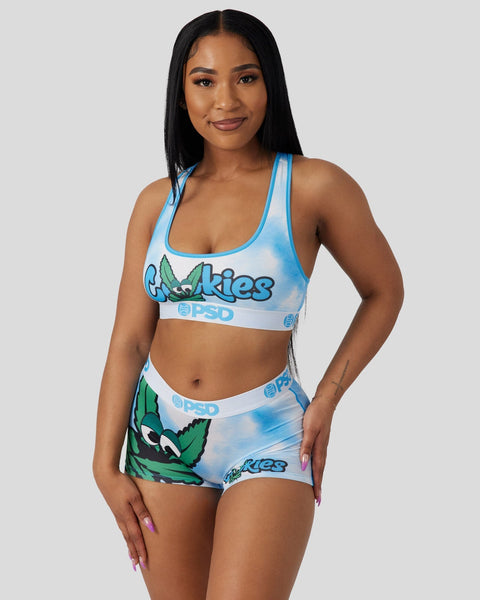Woman wearing blue and white Cookies-branded sports bra and shorts set with green leaf graphics and PSD waistband.