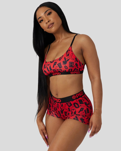 Woman wearing red bra and briefs set with black letter and logo print throughout.