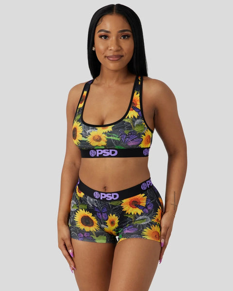 Woman wearing black sports bra and shorts set with yellow sunflower and purple floral print, PSD waistband.