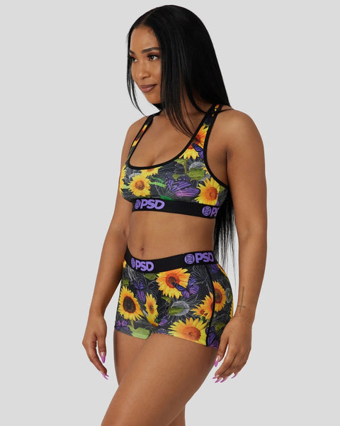 Woman wearing black sports bra and shorts with yellow sunflower and purple butterfly print, PSD waistband visible.