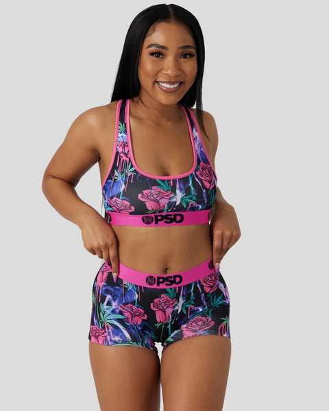 Woman wearing black sports bra and shorts with pink floral print and hot pink trim, featuring PSD branding on waistband.