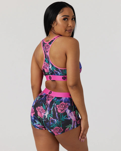 Woman wearing two-piece athletic set with floral rose print in pink, purple, and teal with matching sports bra and shorts.