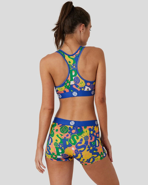 Woman wearing colorful blue, yellow, and green patterned sports bra and shorts set with abstract shapes.