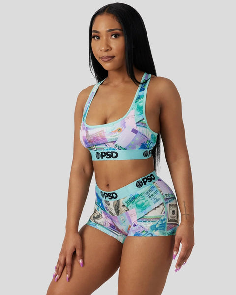 Woman wearing multicolored currency-print sports bra and shorts set with turquoise PSD branding.