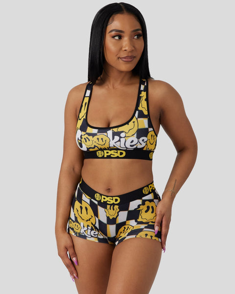 Woman wearing yellow and black smiley face print sports bra and matching shorts with PSD branding.