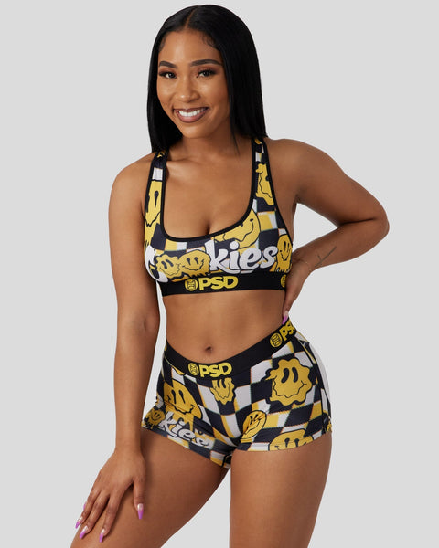 Woman wearing yellow smiley face print sports bra and shorts set with black trim and PSD branding.