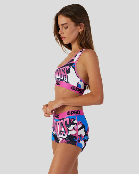 Woman wearing pink, blue, and black camouflage print sports bra and shorts set with PSD branding.