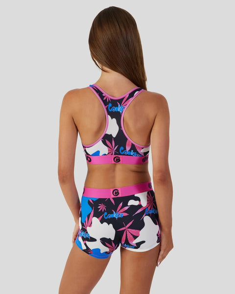 Woman wearing Cookies brand sports bra and shorts set with black, pink, blue and white camouflage leaf print pattern, shown f