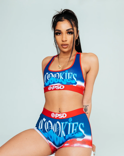 Woman wearing blue and red Cookies sports bra and shorts set with PSD branding against light gray background.