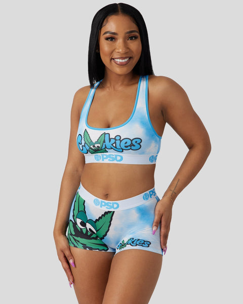 Woman wearing blue and white Cookies sports bra and shorts set with green leaf graphics and PSD branding.