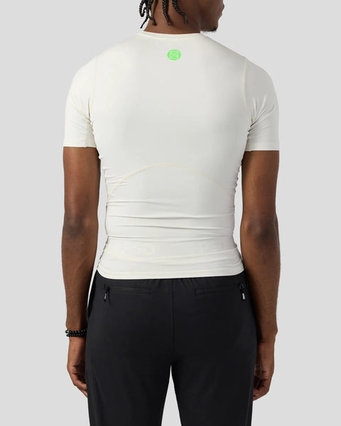 White short-sleeve compression tee with small green circular logo on back, fitted design visible on torso.