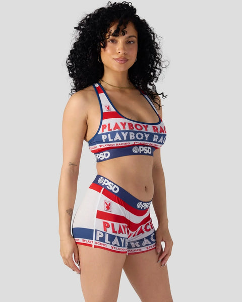 Woman wearing Playboy Racing red, white, and navy sports bra and matching shorts with logo text and stripes.