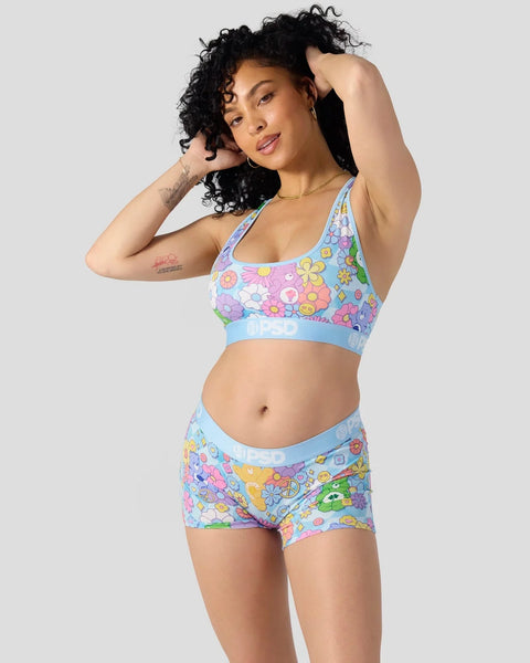 Woman wearing Care Bears-patterned light blue sports bra and matching shorts with colorful flower and character graphics.