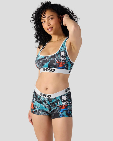 Woman wearing Simpsons-themed sports bra and shorts set with skull and character print in turquoise and black.