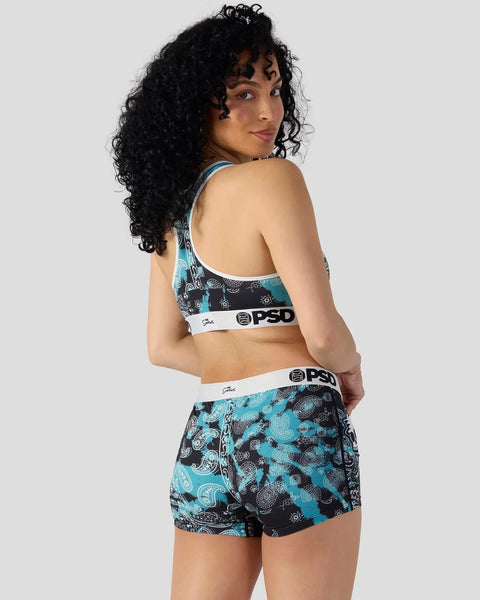 Woman wearing turquoise and black patterned sports bra and shorts set with PSD branding.