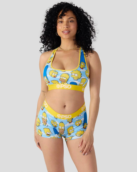 Woman wearing The Simpsons character print sports bra and shorts set with yellow waistband on gray background.