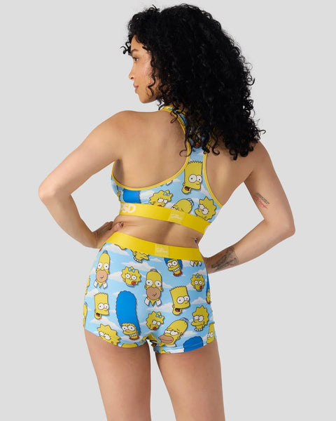 Woman wearing yellow and blue sports bra and shorts set with repeated Simpsons character heads pattern.