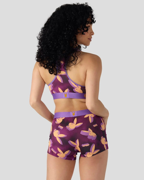 Woman wearing purple sports bra and shorts with gold and orange bunny print pattern, shown from back view.