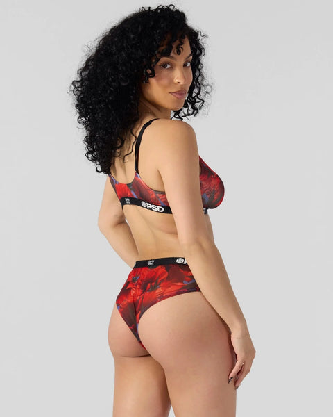 Woman wearing red and black poppy-patterned sports bra and briefs set with black straps and branding.