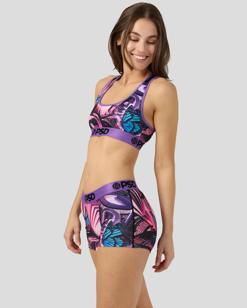 Woman wearing purple sports bra and matching shorts with butterfly and abstract print design.