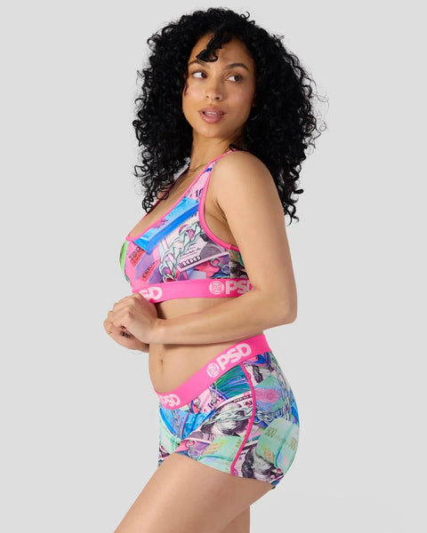 Woman wearing pink sports bra and matching shorts with colorful graphic print and elastic waistband.