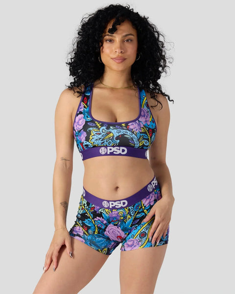 Woman wearing purple sports bra and shorts with colorful paisley and floral pattern, featuring PSD branding on waistband.