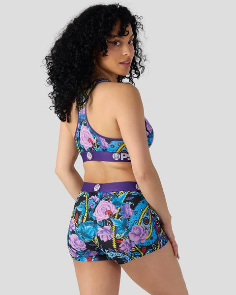 Woman wearing purple sports bra and matching shorts with violet paisley floral print on blue background.