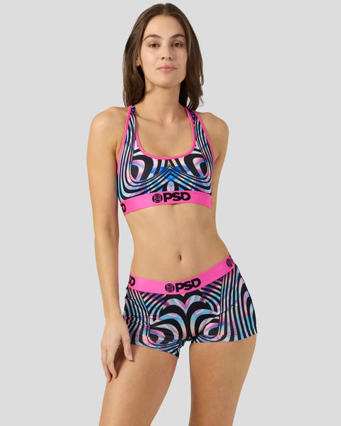 Woman wearing a two-piece swimsuit with neon pink waistbands and black, blue, and white geometric patterns throughout.