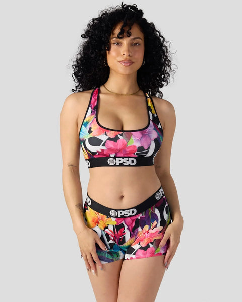 Woman wearing black sports bra and shorts with multicolored floral print and PSD branding.