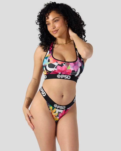 Woman wearing a colorful floral sports bra and matching briefs with black trim and branding.