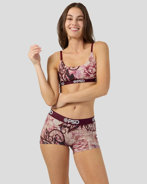 Woman wearing burgundy and pink jacquard patterned sports bra and matching boy shorts with branded waistband.