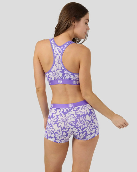 Purple sports bra and shorts set with white floral pattern, shown on model from back view.
