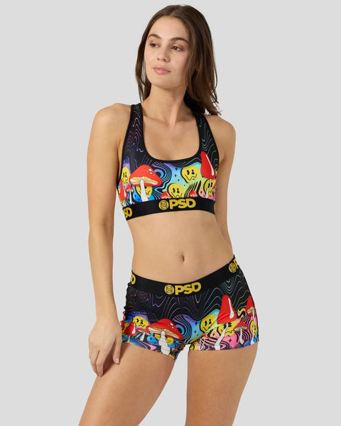 Woman wearing black sports bra and shorts with colorful mushroom and smiley face print, PSD waistband.