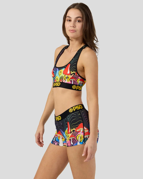Woman wearing colorful mushroom-print sports bra and matching shorts with black elastic waistband and PSD branding.
