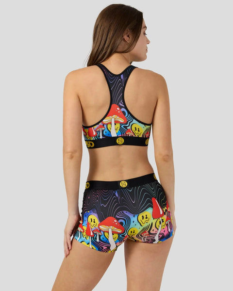 Woman wearing colorful mushroom-print sports bra and matching shorts with black waistband and trim.
