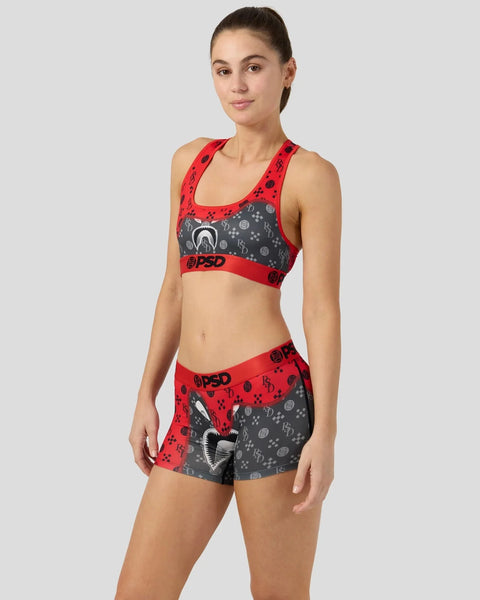 Woman wearing red and gray patterned sports bra and matching shorts with graphic design and branding.