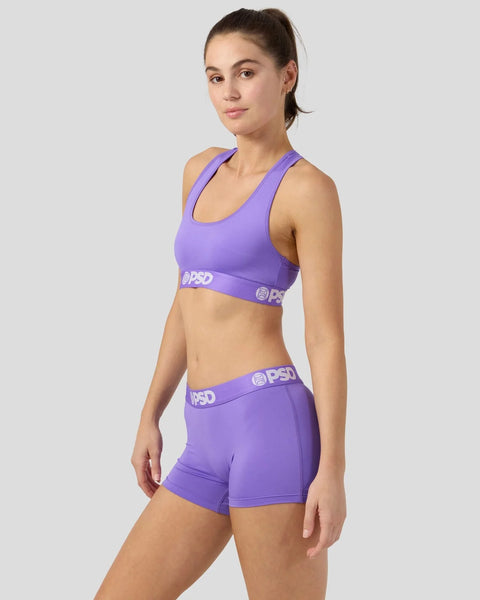 Woman wearing purple sports bra and matching shorts with PSD branding on elastic waistband.