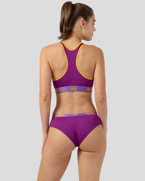 Woman wearing purple sports bra and briefs with gold trim and branded waistband, shown from back.